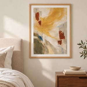 May include: A framed abstract wall art print featuring a textured composition of mustard yellow, deep red, olive green, and soft grey brushstrokes. The artwork is enclosed in a light-toned wooden frame and displayed on a neutral-coloured wall.