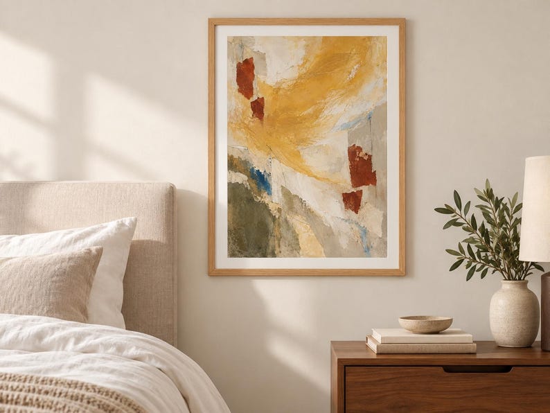 May include: A framed abstract wall art print featuring a textured composition of mustard yellow, deep red, olive green, and soft grey brushstrokes. The artwork is enclosed in a light-toned wooden frame and displayed on a neutral-coloured wall.