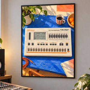May include: A framed wall art print featuring a Roland Rhythm Composer TR-707 drum machine resting on a bright blue table. The image includes a coffee mug, a small bowl of oranges, and a coiled orange cable, all set against a vibrant backdrop.