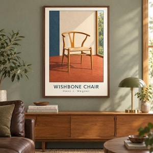 May include: A framed wall art print featuring a light wood Wishbone chair with a woven seat, set against a backdrop of a blue wall, a beige wall, and a window view. The text WISHBONE CHAIR Hans J. Wegner is printed in black at the bottom.