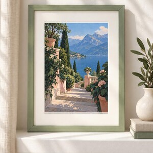 Peut inclure: Une impression d'art encadr&eacute;e repr&eacute;sentant un paysage avec un escalier en pierre menant vers un lac bleu et des montagnes. La sc&egrave;ne comprend des pots en terre cuite avec des fleurs, des cypr&egrave;s et un cadre vert clair avec un passe-partout blanc.