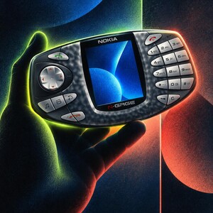 Puede incluir: Una consola de juegos port&aacute;til Nokia N-Gage con una carcasa gris oscuro texturizada. El dispositivo cuenta con una pantalla central a color que muestra un gr&aacute;fico azul abstracto, un pad direccional a la izquierda y un teclado num&eacute;rico a la derecha.