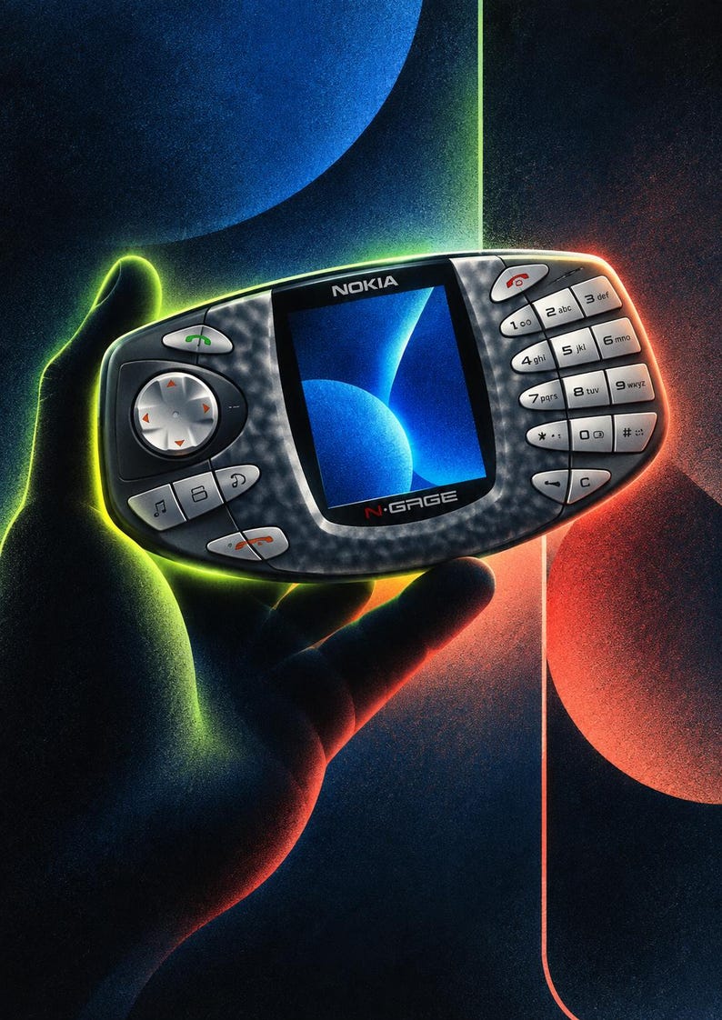 Puede incluir: Una consola de juegos port&aacute;til Nokia N-Gage con una carcasa gris oscuro texturizada. El dispositivo cuenta con una pantalla central a color que muestra un gr&aacute;fico azul abstracto, un pad direccional a la izquierda y un teclado num&eacute;rico a la derecha.