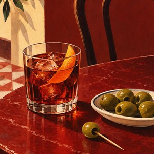 May include: A glass of dark amber liquid with ice cubes and an orange peel garnish sits on a deep red table next to a small white bowl containing five green olives and a single green olive on a wooden toothpick resting on the table surface.