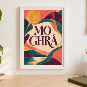 May include: A framed art print featuring a stylized landscape with a large yellow sun, rolling hills in shades of deep purple and teal, and a reflective body of water. The text MO GHR&Aacute; is centered in dark purple lettering against a cream background.