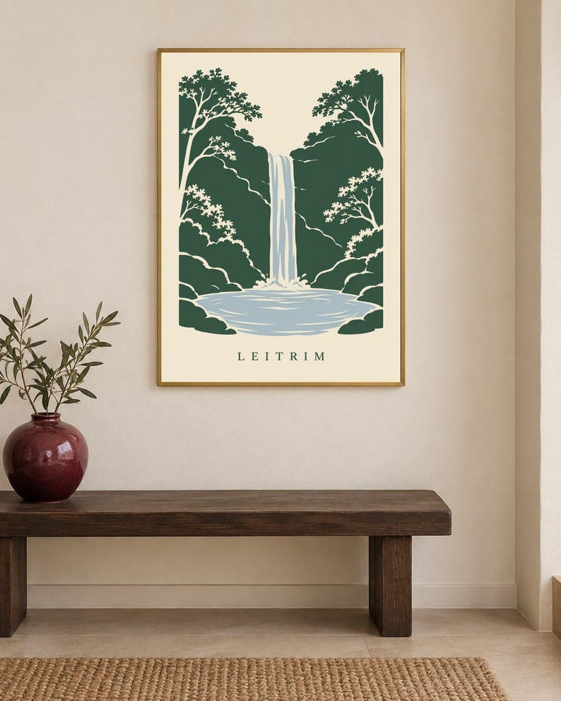K&ouml;nnte beinhalten: Ein rechteckiger Wandkunstdruck in einem goldenen Rahmen mit einer stilisierten Illustration eines Wasserfalls, der in ein Becken st&uuml;rzt, umgeben von dunkelgr&uuml;nen B&auml;umen auf cremefarbenem Grund, mit dem Wort LEITRIM in Schwarz unten.