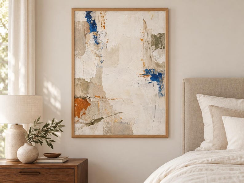 K&ouml;nnte beinhalten: Ein rechteckiges Wandbild in einem hellen Holzrahmen mit einer abstrakten Komposition. Das Kunstwerk zeigt geschichtete Texturen in Off-White-, Creme- und Beiget&ouml;nen, akzentuiert durch kr&auml;ftige Flecken in tiefem Blau und gebranntem Orange.