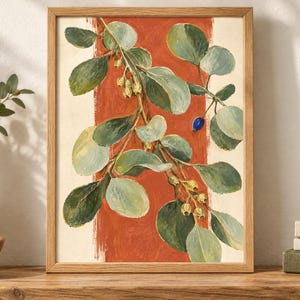May include: A framed botanical print featuring a leafy branch with green foliage and small yellow buds against a vertical terracotta orange stripe on a cream background. The artwork is encased in a light-toned wooden frame with a simple profile.