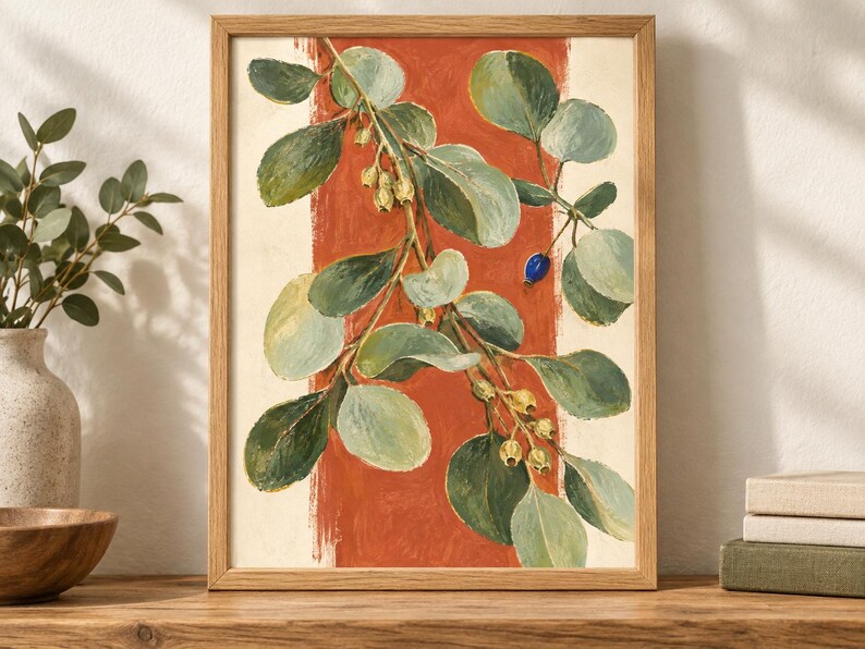 May include: A framed botanical print featuring a leafy branch with green foliage and small yellow buds against a vertical terracotta orange stripe on a cream background. The artwork is encased in a light-toned wooden frame with a simple profile.