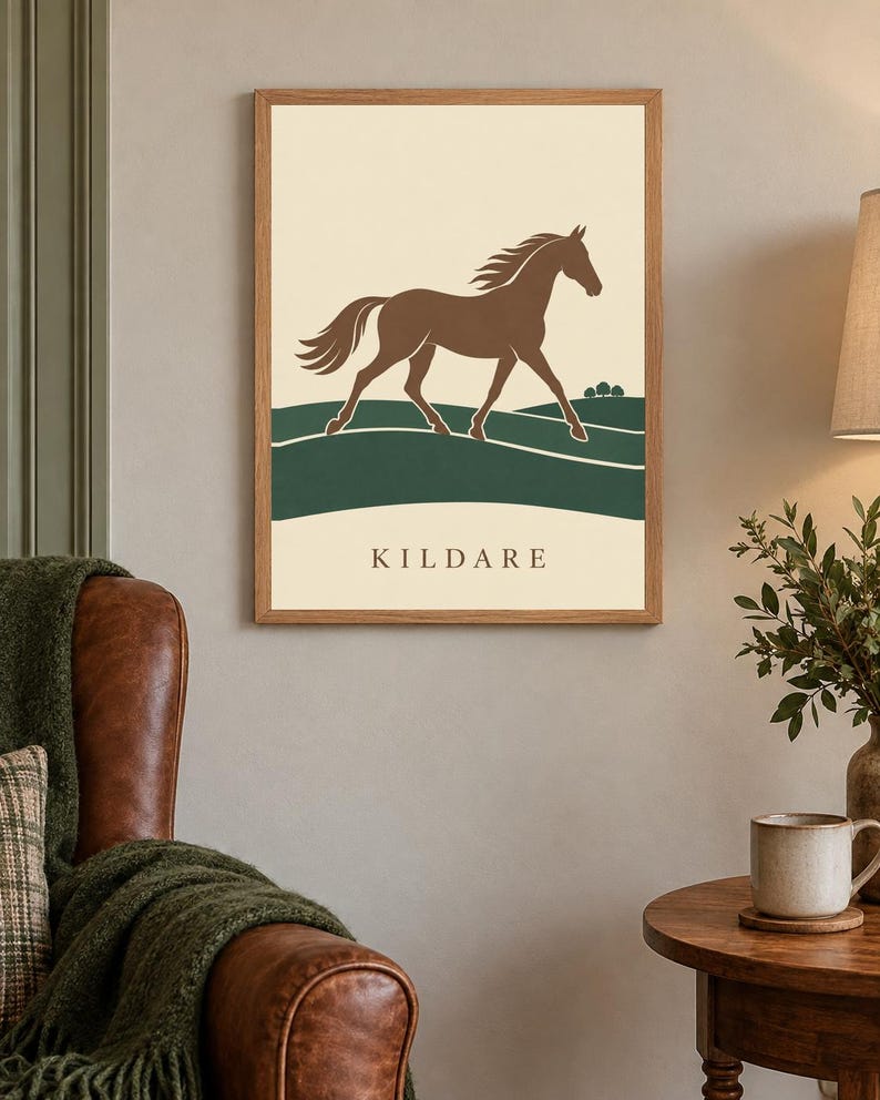 May include: A framed wall art print featuring a brown horse galloping across a dark green landscape against a cream background. The word KILDARE is printed in dark brown capital letters at the bottom of the print, which is encased in a light wood frame.