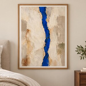 May include: A framed vertical wall art piece featuring a textured, abstract composition. The artwork displays large, layered sections of cream, beige, and tan tones, split down the center by a vibrant, deep blue vertical crevice or river-like shape.