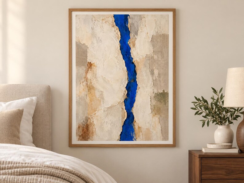 May include: A framed vertical wall art piece featuring a textured, abstract composition. The artwork displays large, layered sections of cream, beige, and tan tones, split down the center by a vibrant, deep blue vertical crevice or river-like shape.