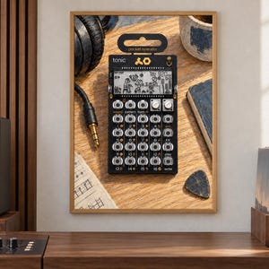 May include: A black Teenage Engineering PO-32 Tonic pocket operator synthesizer featuring a monochrome LCD screen with animated graphics, a grid of sixteen silver buttons, two rotary knobs, and the text "tonic" and "pocket operator" printed on the front.