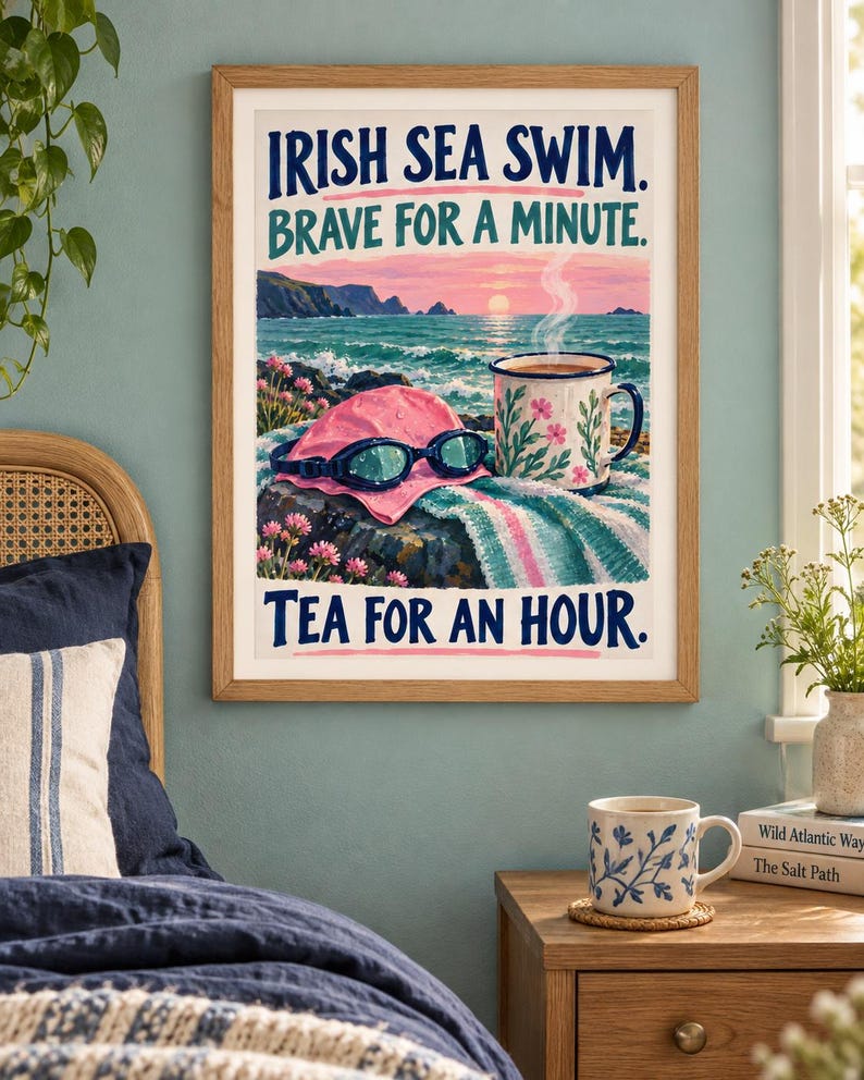 May include: A framed wall art print featuring a coastal scene with a pink swim cap, blue goggles, and a floral mug on a rock. The text reads IRISH SEA SWIM. BRAVE FOR A MINUTE. TEA FOR AN HOUR. The illustration includes a sunset over the ocean.