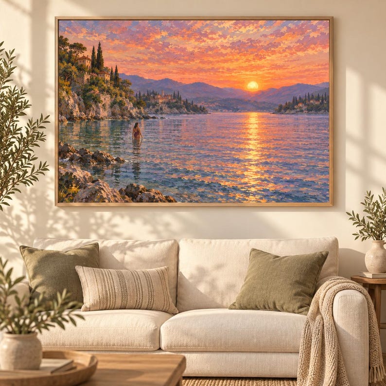 May include: A rectangular framed landscape painting depicting a coastal scene at sunset with vibrant orange and pink clouds, a bright sun over distant mountains, calm water reflecting the light, rocky cliffs, and a figure wading in the sea.