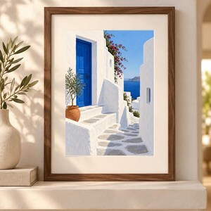 Puede incluir: Una l&aacute;mina de arte enmarcada que representa una escena mediterr&aacute;nea con edificios de piedra blanca, una puerta azul vibrante, una maceta de terracota con un peque&ntilde;o olivo, flores de buganvilla rosa y vistas al mar azul bajo un cielo despejado.