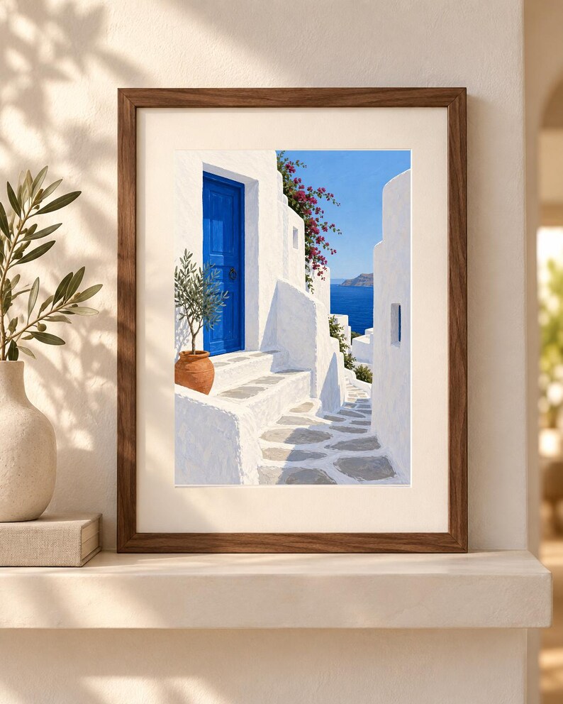 Puede incluir: Una l&aacute;mina de arte enmarcada que representa una escena mediterr&aacute;nea con edificios de piedra blanca, una puerta azul vibrante, una maceta de terracota con un peque&ntilde;o olivo, flores de buganvilla rosa y vistas al mar azul bajo un cielo despejado.