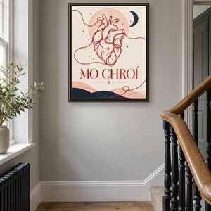 May include: A framed wall art print featuring a red line-art anatomical heart centered against a pale background with a crescent moon, stars, and dark blue hills at the bottom. The text MO CHRO&Iacute; is printed in red below the heart illustration.