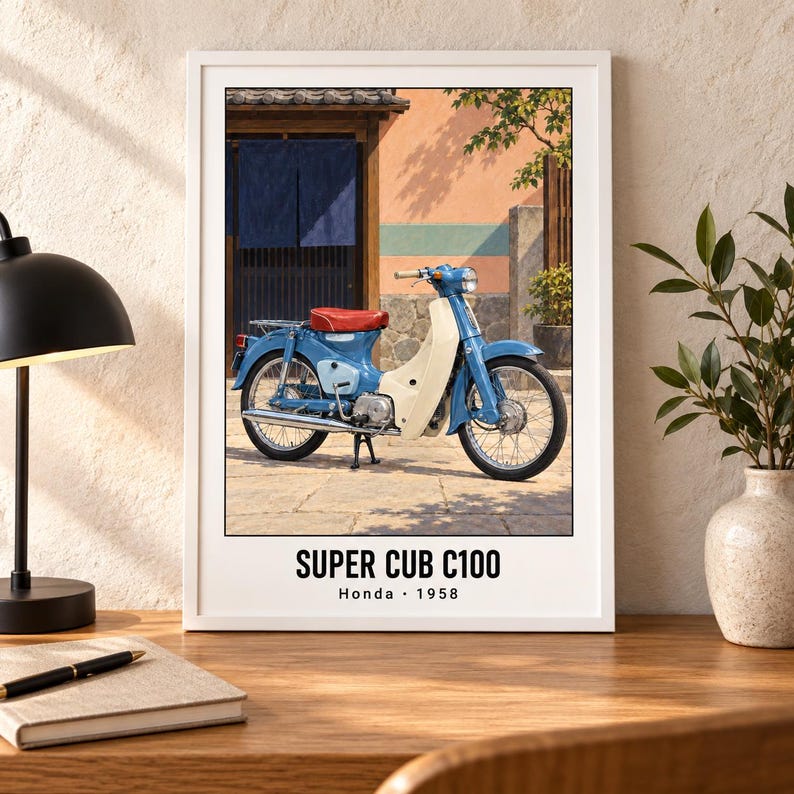 May include: A framed wall art print featuring a blue and cream Honda Super Cub C100 motorcycle from 1958. The motorcycle has a red seat and is parked on a stone surface in front of a building with blue curtains. The text reads SUPER CUB C100 Honda 1958.