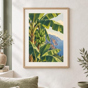 May include: A framed vertical art print featuring a vibrant green banana tree with a large bunch of bananas in the foreground, set against a coastal landscape with blue ocean waters, rocky cliffs, and a pale sky with soft clouds in the background.