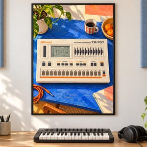 May include: A framed wall art print featuring a Roland TR-707 Rhythm Composer drum machine. The device is light beige with orange accents, a digital display, and multiple sliders. It sits on a bright blue table with a coffee mug and oranges.