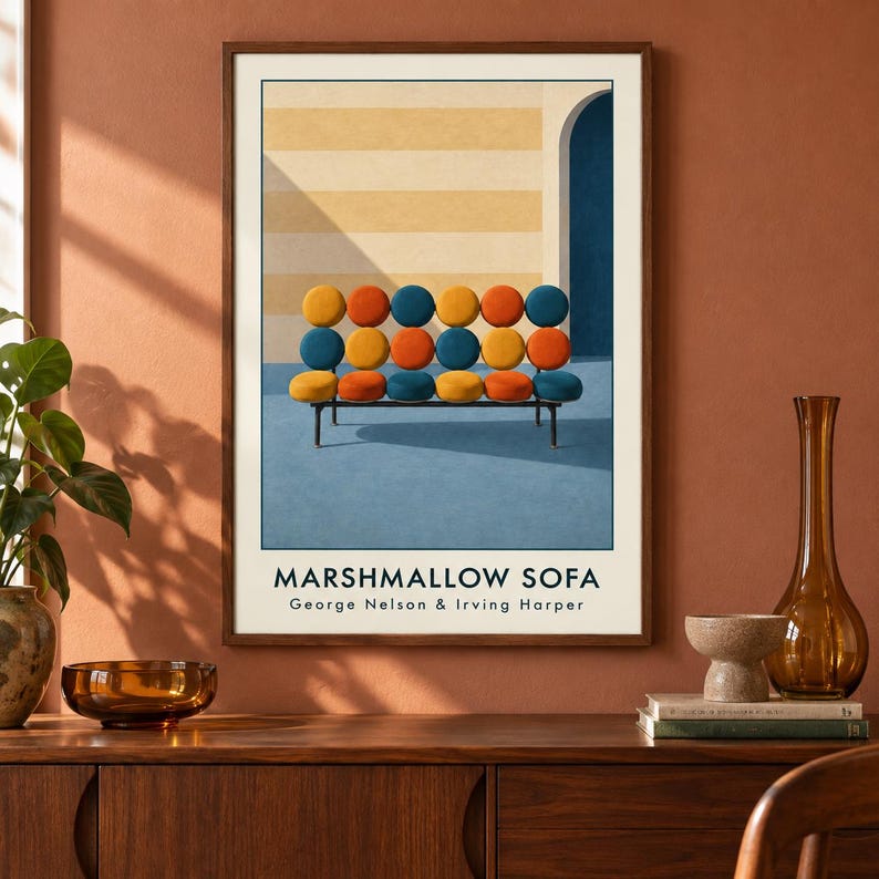 May include: A framed art print titled MARSHMALLOW SOFA by George Nelson & Irving Harper. The print features a graphic illustration of a sofa with eighteen circular cushions in yellow, orange, and blue, set against a striped wall and blue floor.