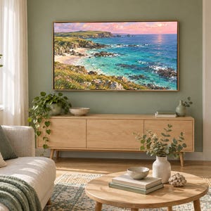 May include: A rectangular landscape painting featuring a coastal scene with turquoise water, rocky cliffs, and green hills under a soft pink and blue sky, displayed in a thin wooden frame mounted on a sage green wall above a light wood media console.