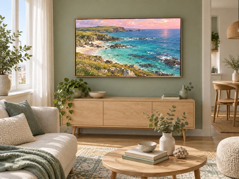May include: A rectangular landscape painting featuring a coastal scene with turquoise water, rocky cliffs, and green hills under a soft pink and blue sky, displayed in a thin wooden frame mounted on a sage green wall above a light wood media console.