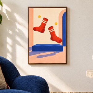 May include: A framed rectangular wall art print featuring two red socks with white stripes floating above a solid blue rectangular platform. The background consists of a light peach wall with a blue archway and two small yellow circles.