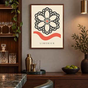 K&ouml;nnte beinhalten: Ein gerahmter Kunstdruck mit cremefarbenem Hintergrund und einem dunkelgrauen, symmetrischen, blumenartigen geometrischen Muster in der Mitte. Darunter befindet sich eine horizontale, wellenf&ouml;rmige korallenrote Linie und das Wort LIMERICK.