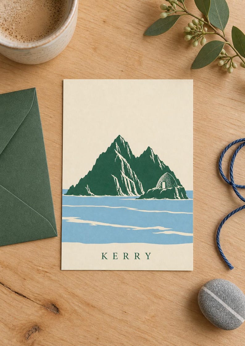 Pu&ograve; includere: Un biglietto d'auguri rettangolare con un'illustrazione serigrafata di montagne verdi e una capanna di pietra a forma di alveare che emerge dall'acqua blu. La parola KERRY &egrave; stampata in lettere maiuscole verde scuro al centro della base del biglietto.