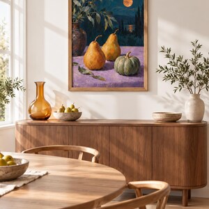 May include: A framed oil painting depicting a still life with two yellow pears and a green pumpkin on a purple surface, set against a dark blue night landscape with a full moon, displayed on a wall above a wooden sideboard with decor items.