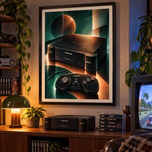 Puede incluir: Una l&aacute;mina de arte mural enmarcada que muestra una consola de juegos Panasonic REAL 3DO negra y su mando a juego. La obra presenta la consola y el mando sobre un fondo geom&eacute;trico oscuro con acentos de luz en tonos naranja c&aacute;lido y azul cerceta.