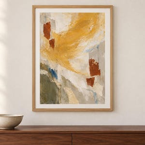 May include: A framed abstract wall art print featuring a textured composition of mustard yellow, burnt orange, olive green, and cream white brushstrokes. The artwork is enclosed in a light-toned wooden frame, displaying a layered, painterly aesthetic.