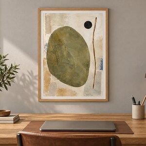 K&ouml;nnte beinhalten: Ein gerahmter abstrakter Wandkunstdruck mit einer gro&szlig;en olivgr&uuml;nen ovalen Form, einem kleinen schwarzen Kreis und einer d&uuml;nnen vertikalen braunen Linie vor einem strukturierten Hintergrund aus beigen, grauen und blauen Pinselstrichen.