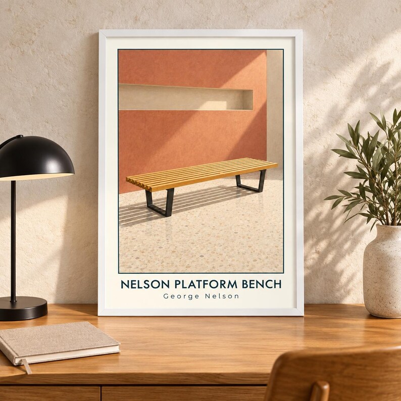 May include: A framed art print featuring a slatted wooden bench with black metal legs set against a terracotta wall. The text at the bottom reads NELSON PLATFORM BENCH and George Nelson. The print is displayed in a white frame on a wooden desk.