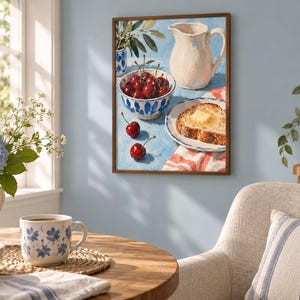 May include: A framed wall art print depicting a still life scene with a white ceramic pitcher, a bowl filled with red cherries, and a slice of buttered toast on a plate, all set against a light blue background with a red and white striped cloth.