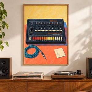 Op de afbeelding: Een ingelijste kunstdruk met een zwarte Roland Rhythm Composer TR-808 drumcomputer met een rij kleurrijke knoppen, een blauwe opgerolde audiokabel en een klein vierkant briefje tegen een levendige gele, oranje en blauwe achtergrond.