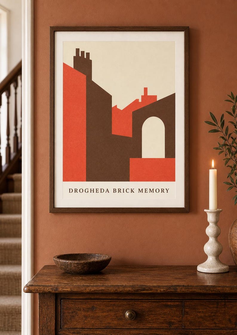 K&ouml;nnte beinhalten: Ein gerahmter Kunstdruck mit einer geometrischen architektonischen Illustration von Geb&auml;uden in Rot-, Braun- und Cremet&ouml;nen. Der Text DROGHEDA BRICK MEMORY ist in Schwarz am unteren Rand des Drucks zu sehen, der in einem dunklen Holzrahmen steckt.