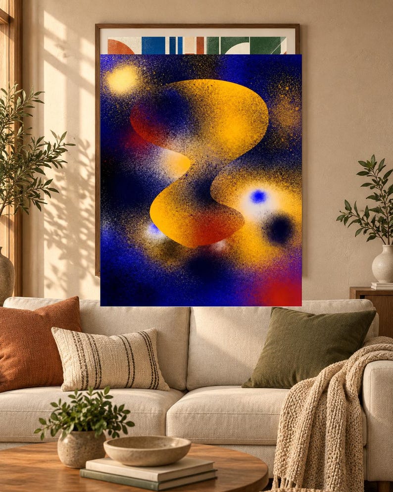 May include: A rectangular wall art print featuring an abstract spray paint design with a central, organic yellow and orange shape set against a deep blue background. The composition includes scattered yellow and white speckles and glowing orbs.