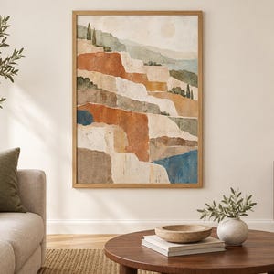 Op de afbeelding: Een verticale rechthoekige wandkunstprint in een lichthouten lijst met een abstract landschapsschilderij. De compositie toont gelaagde terrassen in tinten terracotta, cr&egrave;me, beige en gedempt blauw, geaccentueerd door kleine groene bomen.