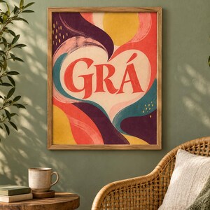 May include: A rectangular framed wall art print featuring a central white heart shape containing the red text GR&Aacute;. The background consists of abstract, flowing shapes in shades of yellow, red, deep purple, and teal with visible brushstroke textures.