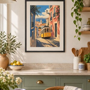 K&ouml;nnte beinhalten: Ein gerahmter Kunstdruck mit einer gelben Stra&szlig;enbahn, die eine gepflasterte Stra&szlig;e zwischen blauen und rosafarbenen Geb&auml;uden entlangf&auml;hrt. Die Szene zeigt eine entfernte Stadt und das Meer unter blauem Himmel in einem lebendigen Malstil.