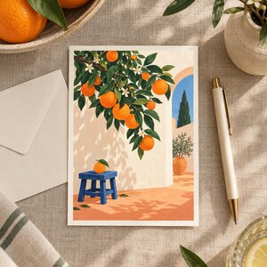 May include: A rectangular art print featuring an illustration of an orange tree with bright fruit and white blossoms hanging over a blue wooden stool. The scene depicts a sunlit courtyard with a terracotta floor, a white wall, and a blue archway.