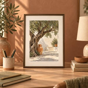 May include: A rectangular framed wall art print featuring a photograph of a gnarled olive tree with green leaves, a terracotta amphora, and a stone patio under bright sunlight, displayed in a dark brown frame with a wide white mat border.