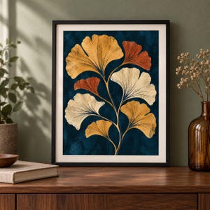 May include: A framed wall art print featuring a botanical illustration of ginkgo biloba leaves in shades of gold, cream, and burnt orange against a deep navy blue textured background. The artwork is enclosed in a simple black frame with a white mat.