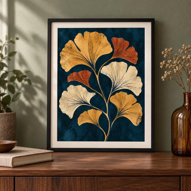 May include: A framed wall art print featuring a botanical illustration of ginkgo biloba leaves in shades of gold, cream, and burnt orange against a deep navy blue textured background. The artwork is enclosed in a simple black frame with a white mat.