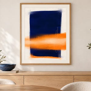 K&ouml;nnte beinhalten: Ein gerahmter abstrakter Wandkunstdruck mit einem gro&szlig;en, vertikalen, dunkel marineblauen rechteckigen Block, der von einem horizontalen, weichkantigen orangefarbenen Band &uuml;berlagert wird. D&uuml;nne, wei&szlig;e, handgezeichnete Linien sind sichtbar.