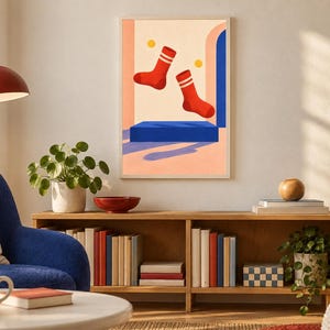 May include: A framed wall art print featuring a graphic illustration of two red socks with white stripes floating above a solid blue rectangular platform, set against a light peach background with yellow circles and blue archway elements.