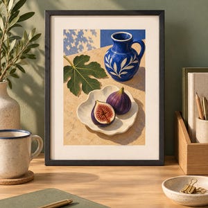 May include: A framed art print featuring a still life painting of a vibrant blue ceramic pitcher with white leaf patterns, a single green fig leaf, and two figs on a scalloped white plate, all set against a warm, sunlit stone surface.